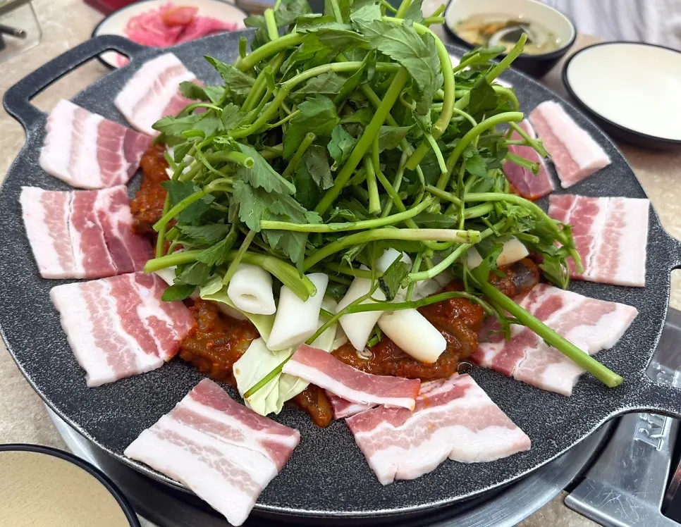 Two servings of griddled jjukkumi with black pork flower pork belly and extra sides