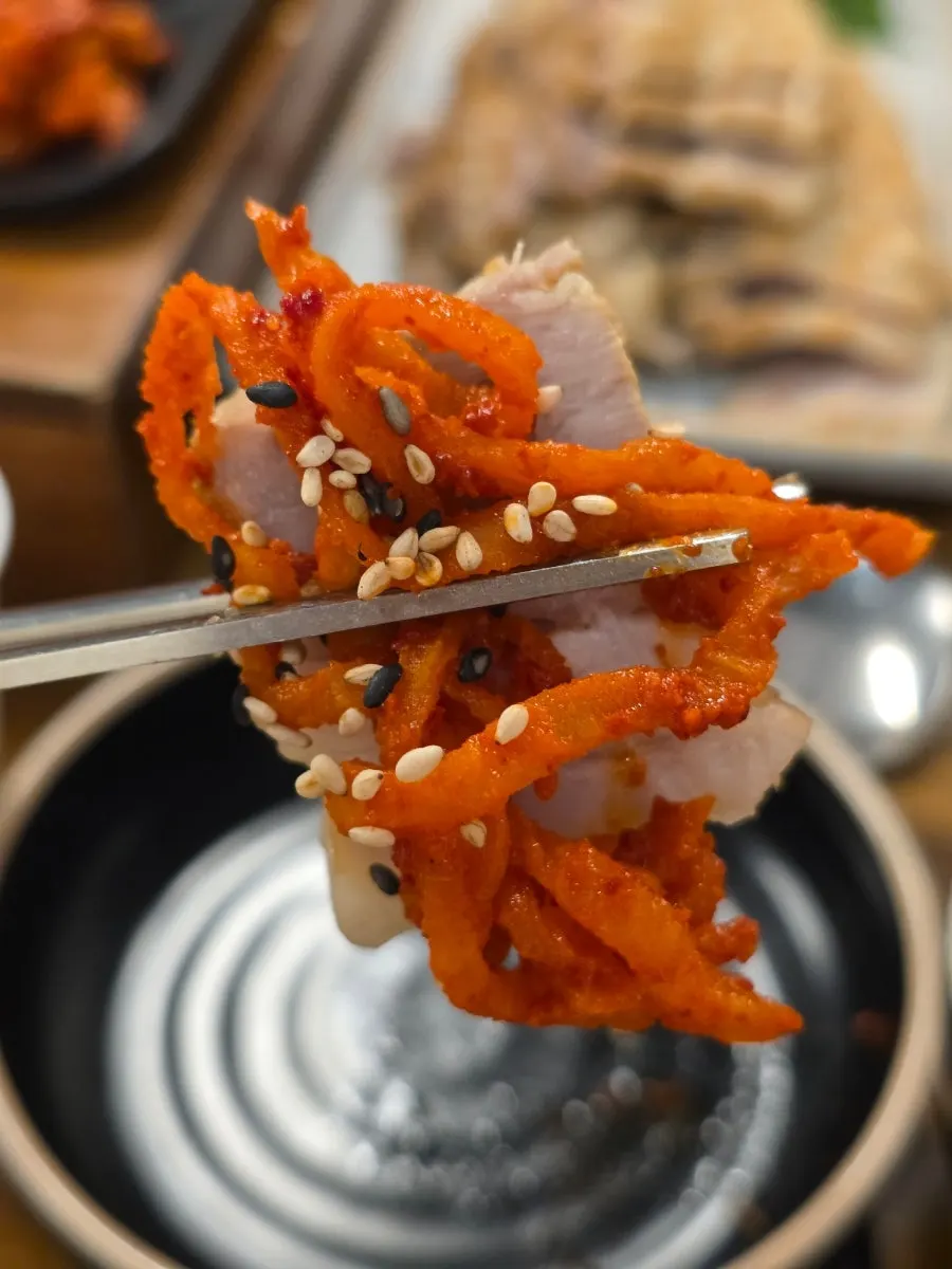 A wrap of bossam topped with fresh kimchi