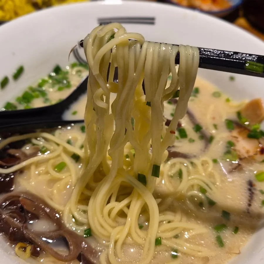 A spoonful of pale tonkotsu broth lifted from the bowl