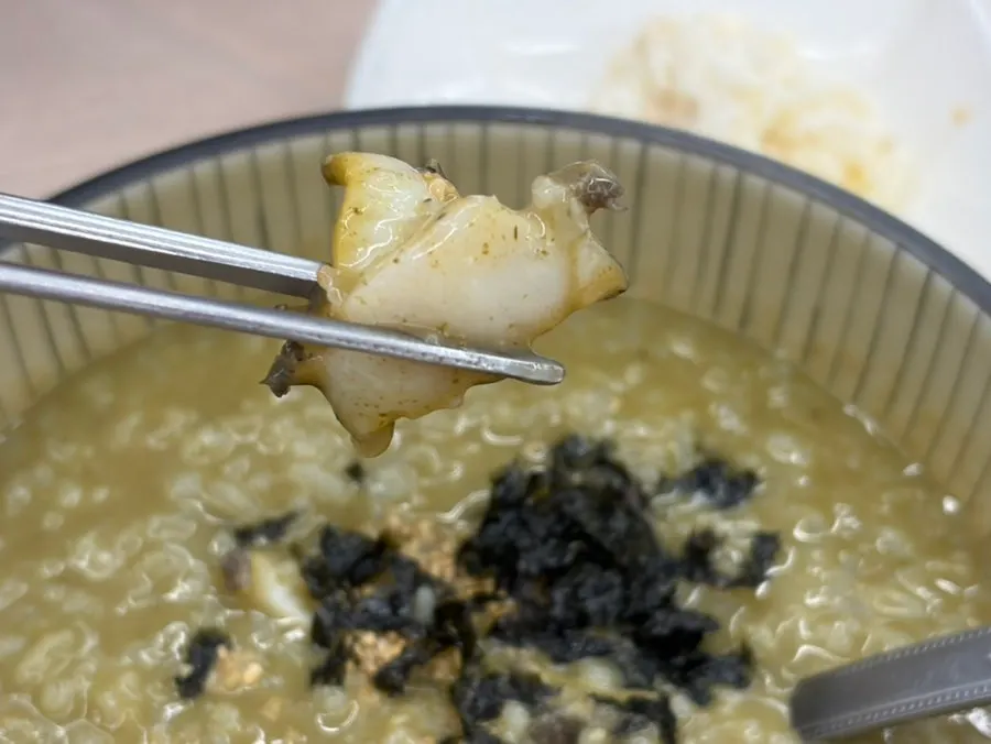 A spoonful of thick abalone porridge lifted from the bowl