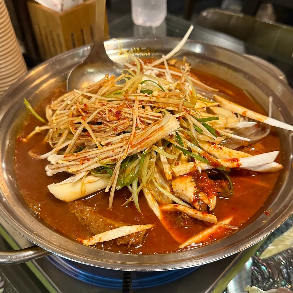 Pot of aged kimchi rib stew topped with shredded green onion, mushrooms, glass noodles, and rice cake