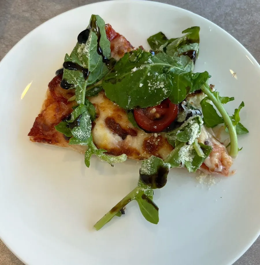 Close-up of a slice of arugula tomato pizza