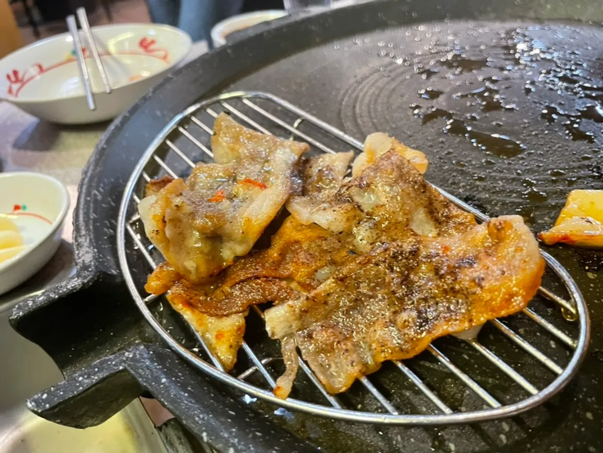 Thin-sliced pork belly cooking on the grill