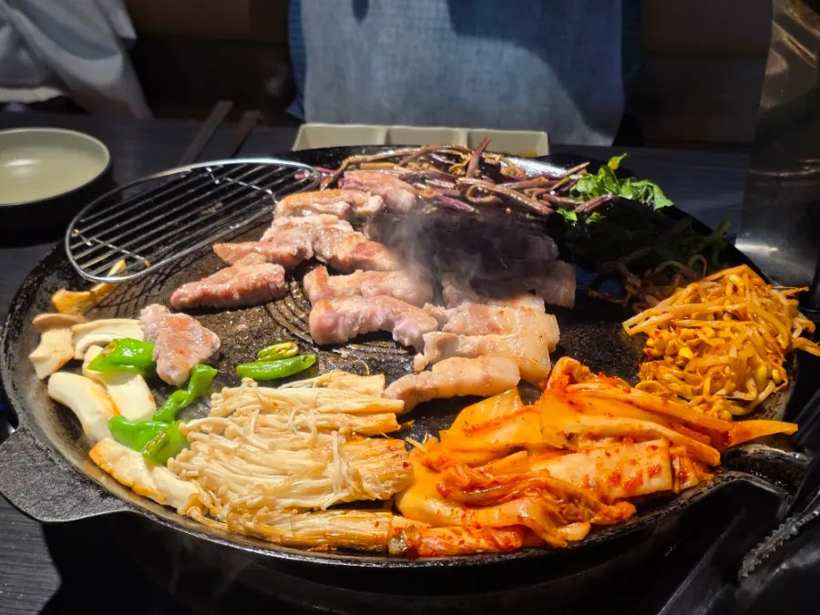 Pork neck and belly grilling with vegetables on the cauldron lid