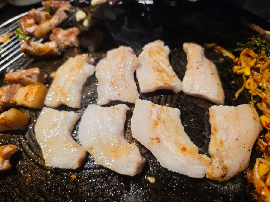 Grilled meat set aside on the edge of the cauldron lid
