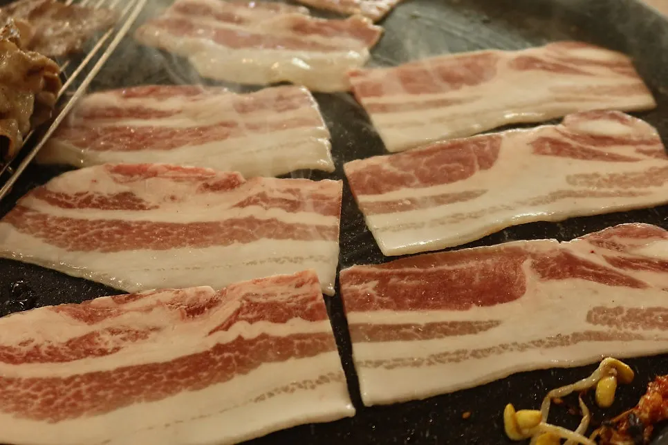 A piece of thin-sliced pork belly with scallion salad and raw garlic