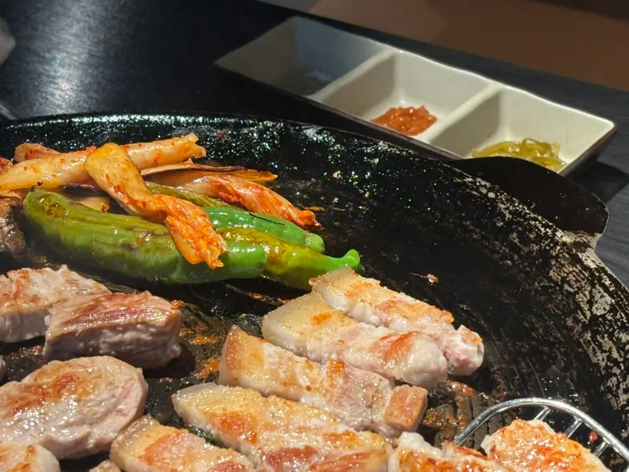 Bright pink pork being grilled by a staff member