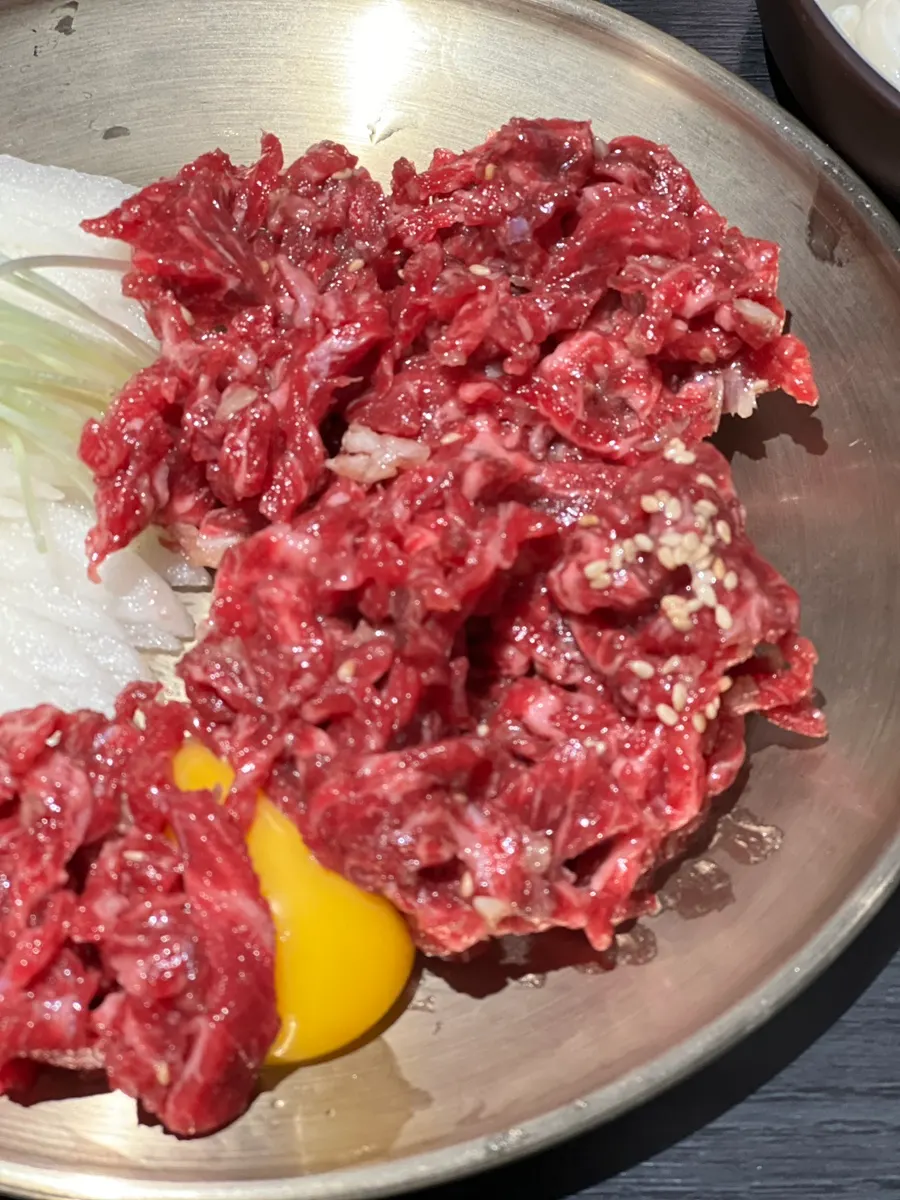 Close-up of yukhoe topped with sesame seeds and minced garlic