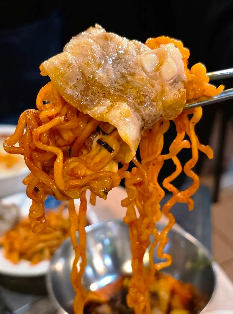 A bite of meat topped with buldak noodles