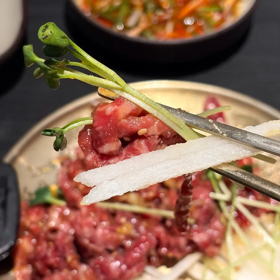 A bite of yukhoe with pear slices and radish sprouts