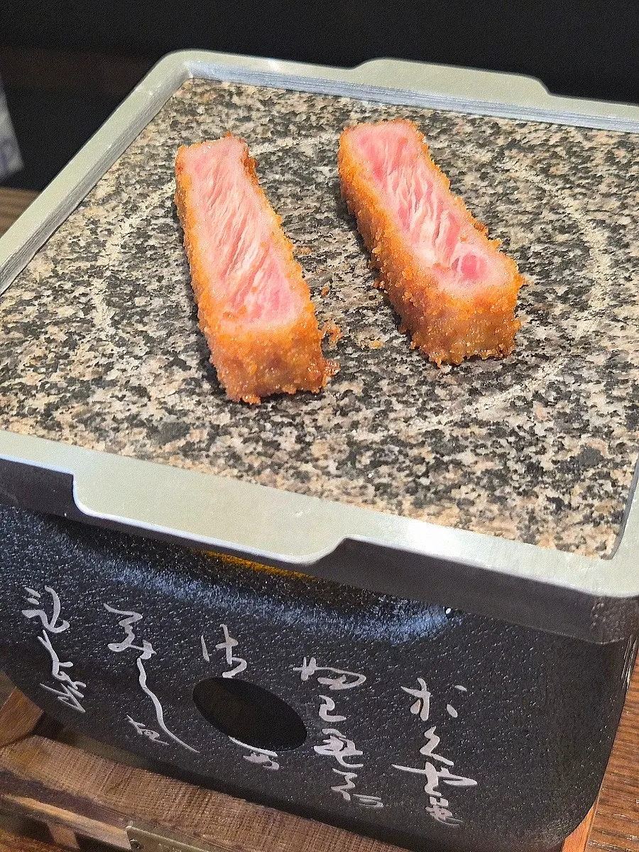Two pieces of gyukatsu grilling on the brazier plate