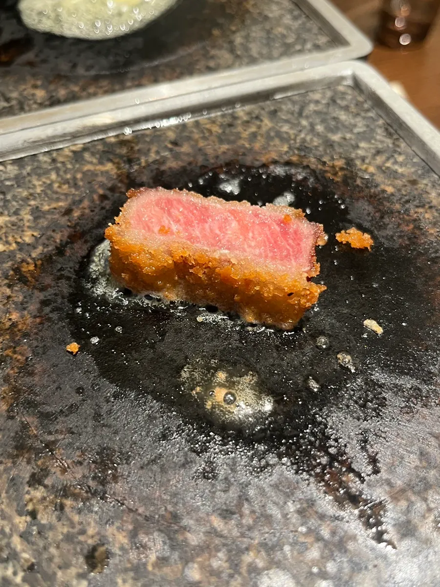 A piece of gyukatsu grilling on the buttered hot plate