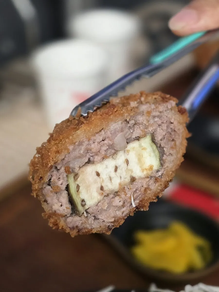 A piece of menchi katsu dipped in sauce