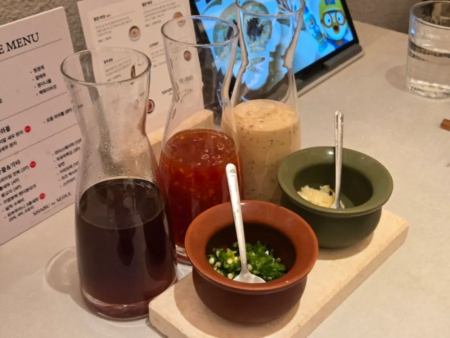 Three sauces — chili sauce, sesame dressing, soy ponzu — with a seasoning jar