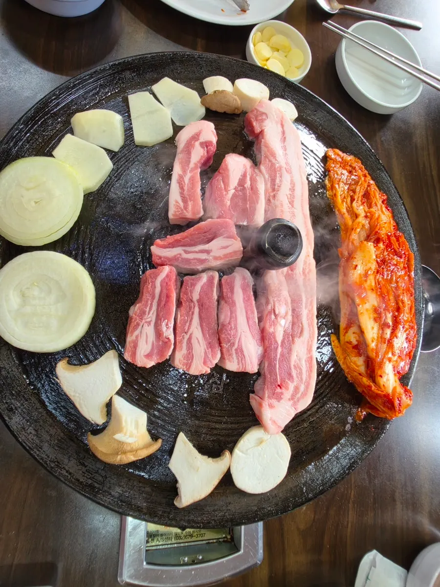 솥뚜껑 위에서 익어가는 고기와 김치