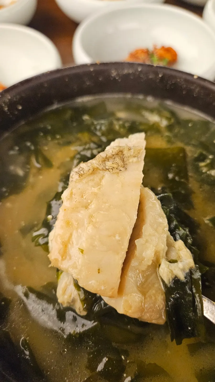 Spoonful of flounder flesh and seaweed lifted from the bowl