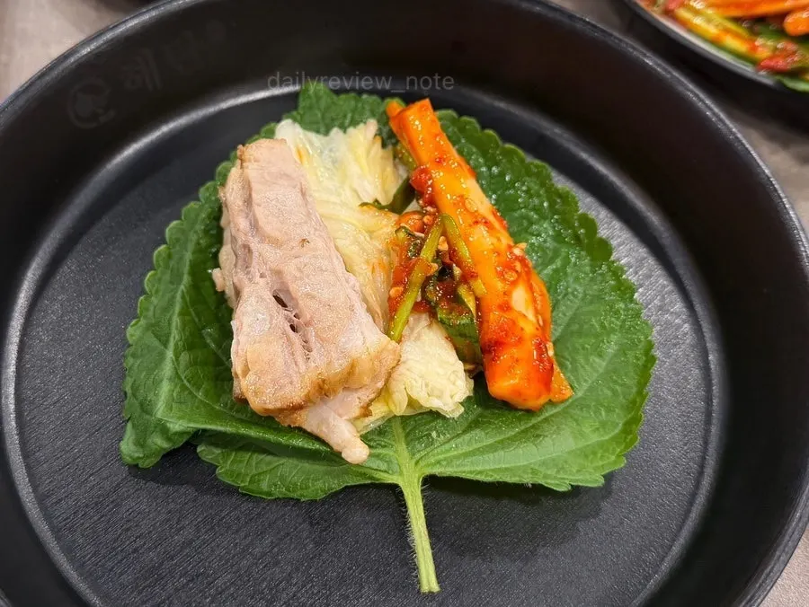A wrap of perilla leaf with boiled pork and spicy squid salad