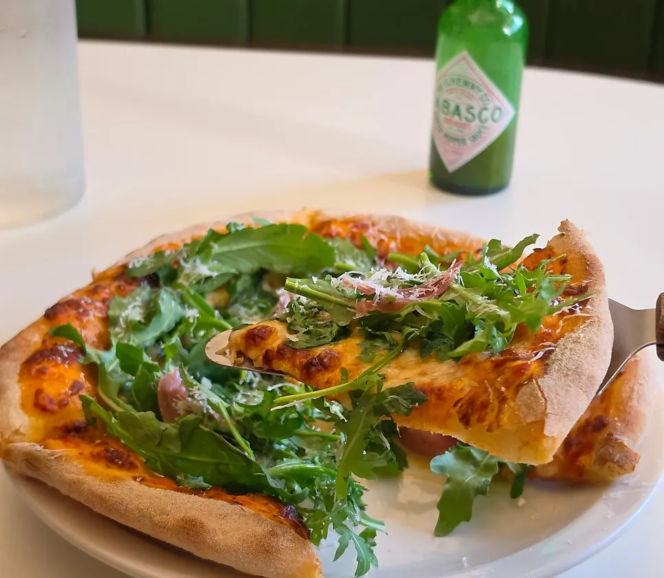 Arugula prosciutto pizza with hot sauce drizzled on top