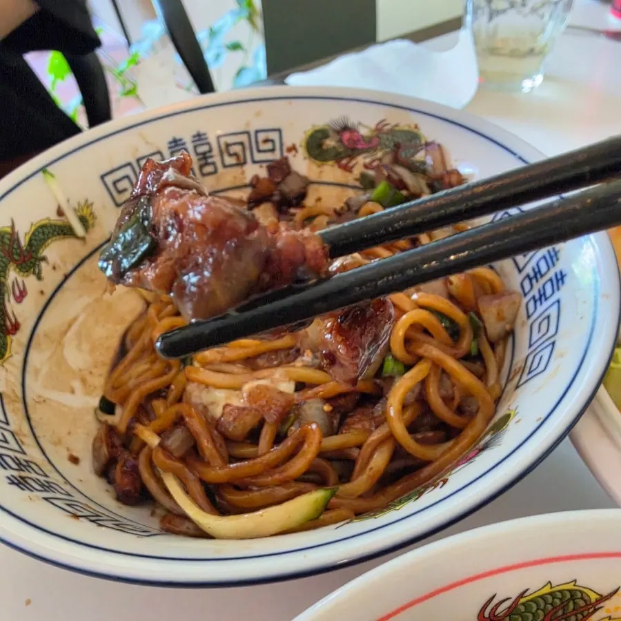 A chopstick-lifted bite of jjajangmyeon noodles