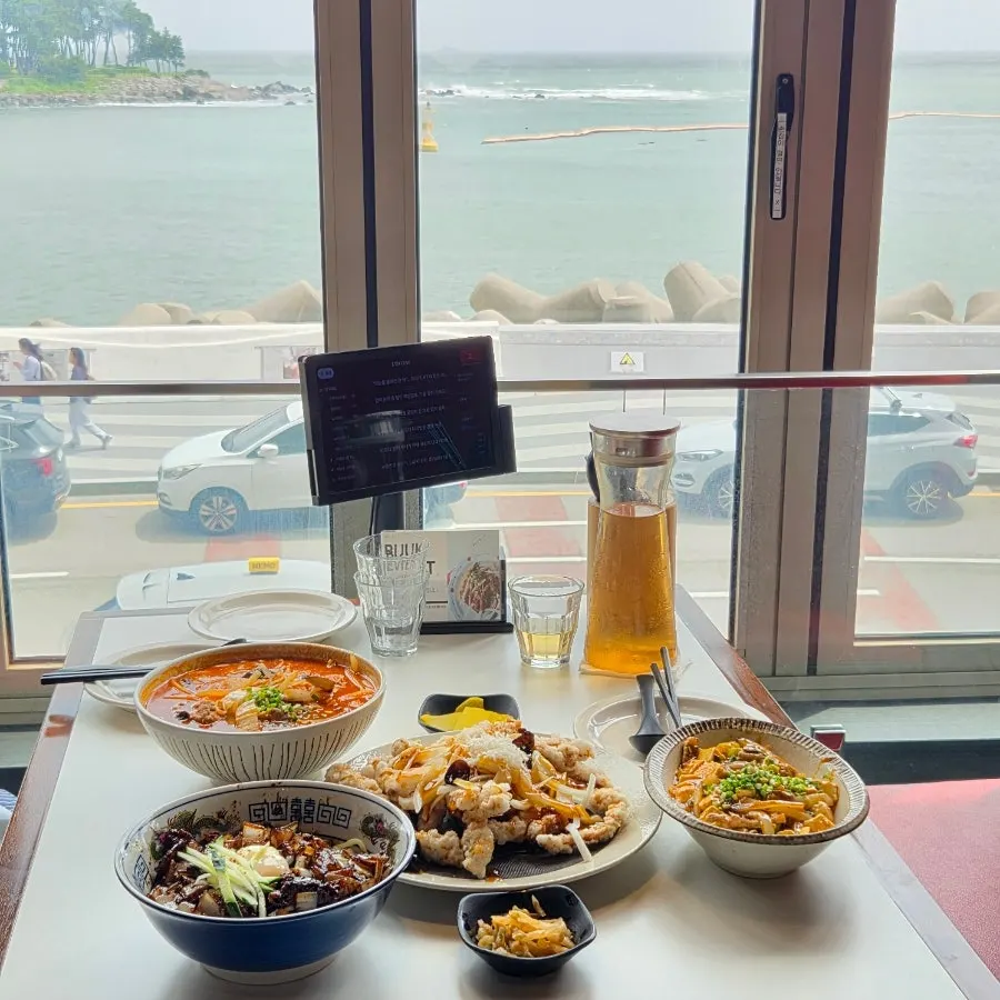 Chinese food spread on a window table with an ocean view