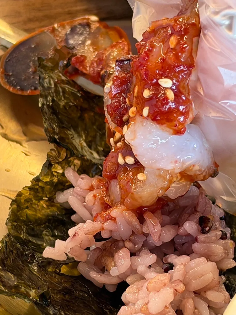 A bite of marinated crab with rice and crab meat on seaweed