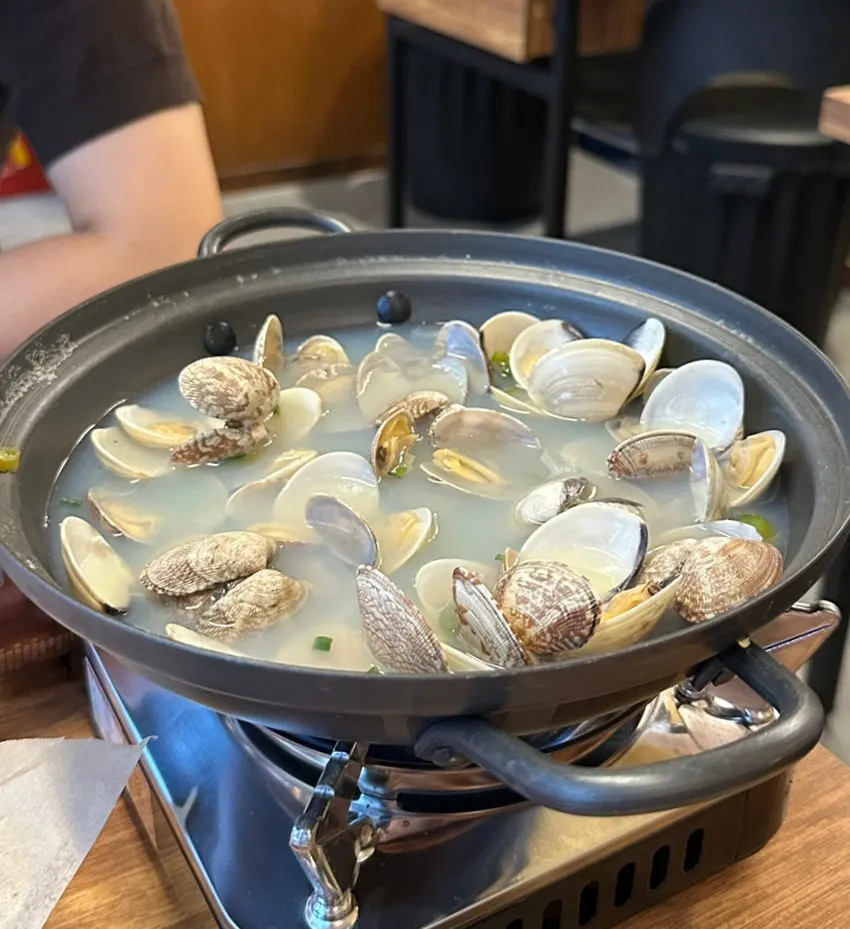 A ladle scooping up clam soup broth and clams