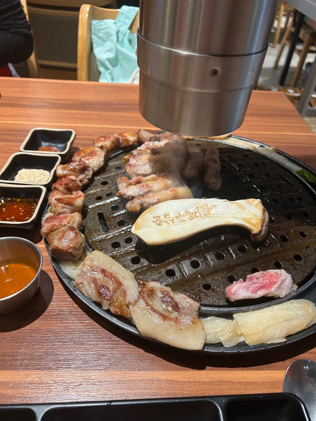 Grilled pork neck and pork belly on the grill with aged kimchi on the side