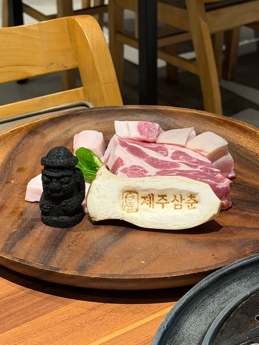 도마에 담긴 흑돼지 목살과 오겹살, 돌하르방 숯 장식