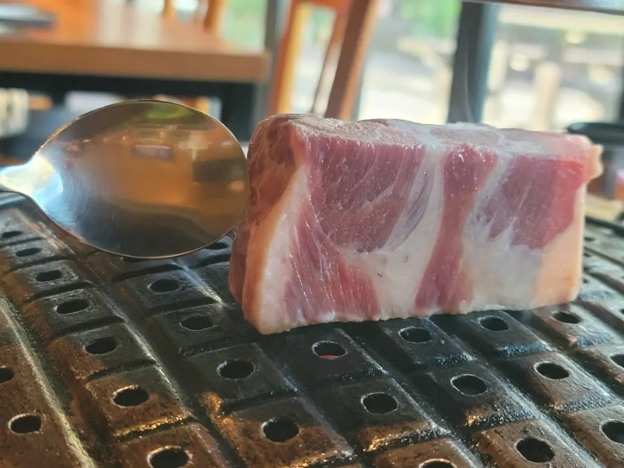 Thickly sliced pork neck cooking on the grill