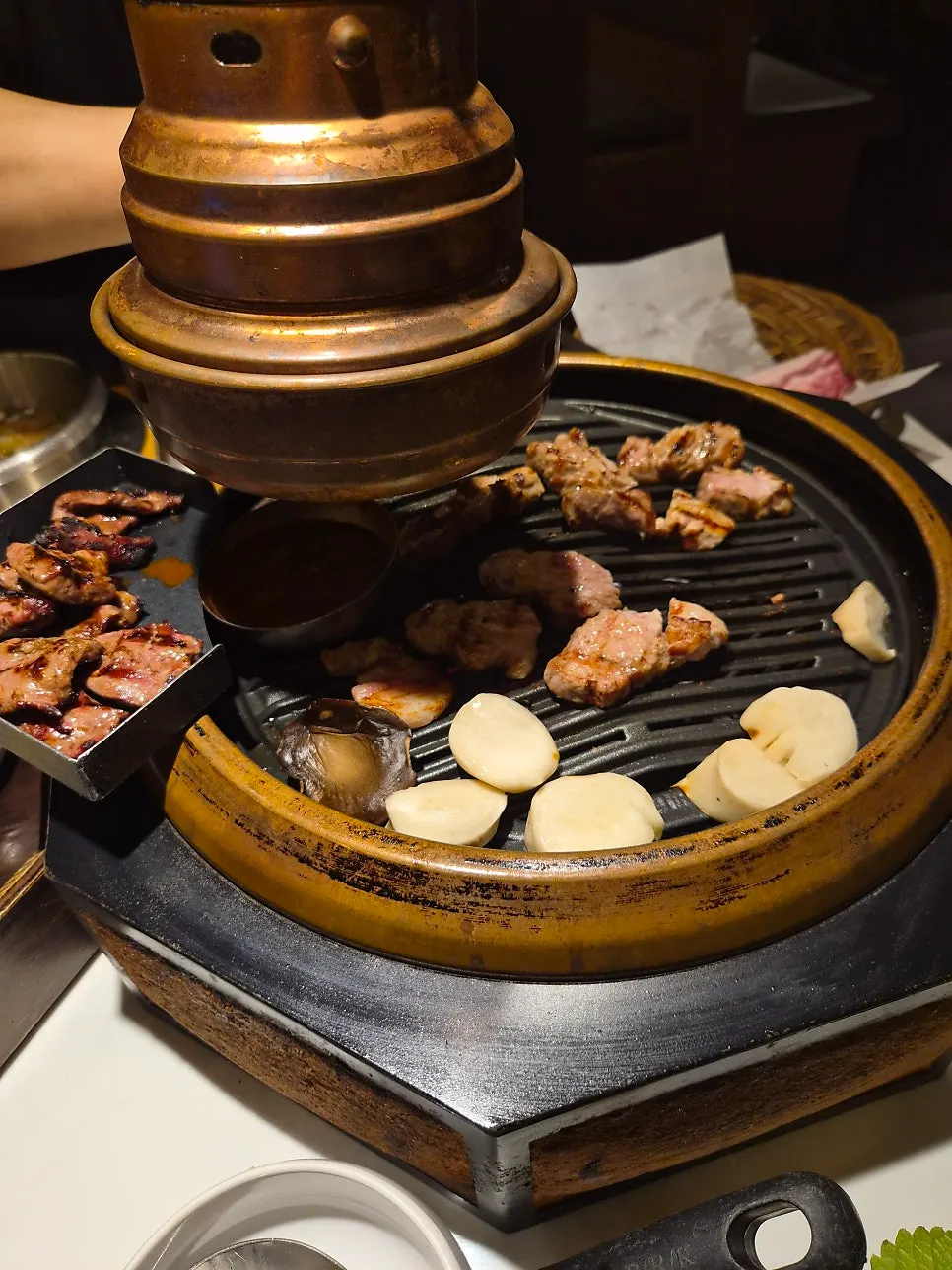 Meat grilling on the pan alongside salted anchovy sauce and king oyster mushrooms