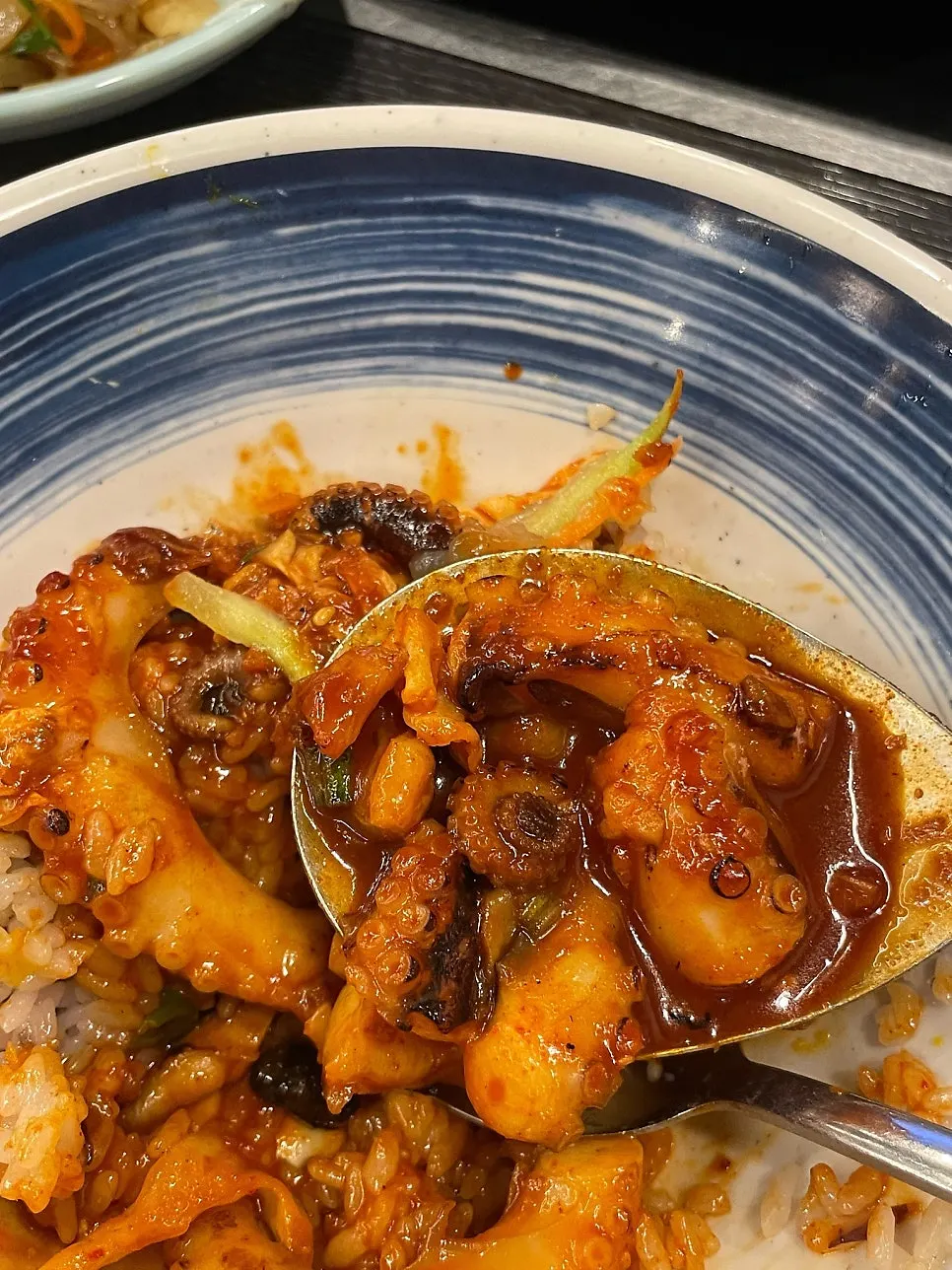 A spoonful of jjukkumi over hot pot rice drizzled with perilla oil