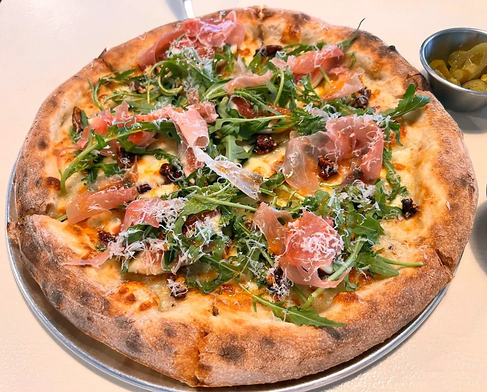 Fig prosciutto wood-fired pizza topped with arugula