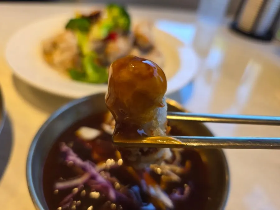 A piece of sweet and sour pork lifted with chopsticks