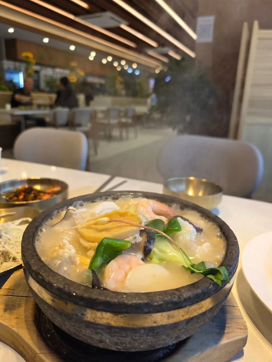 Nurungjitang topped with abalone, seafood, and a small wild ginseng root