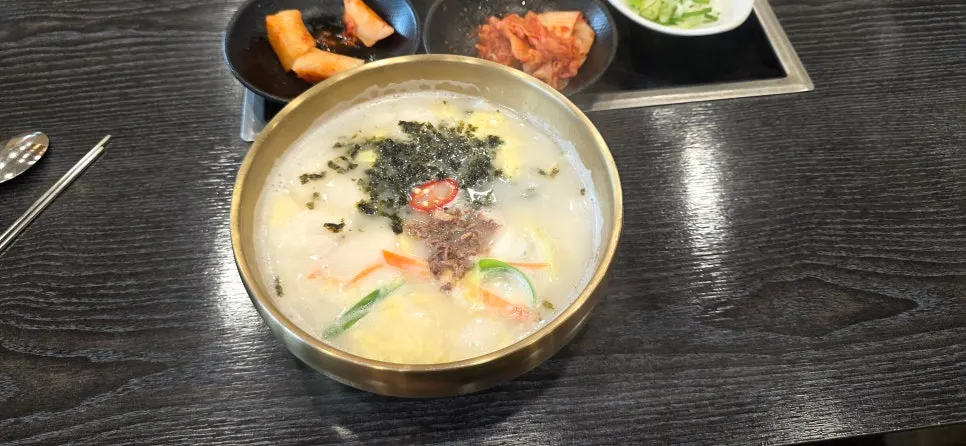 A bowl of tteokguk seolleongtang topped with rice cake, egg, and seaweed flakes