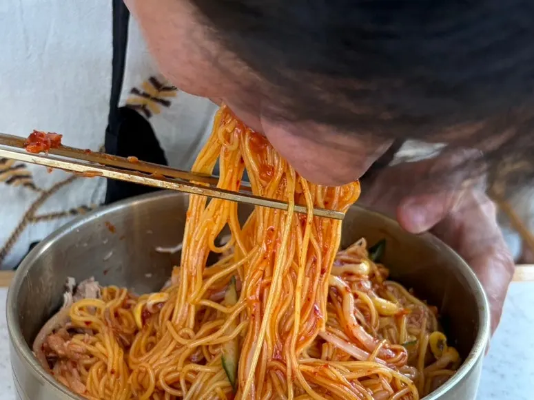 A chopstick-full of bibim noodles piled high with pork