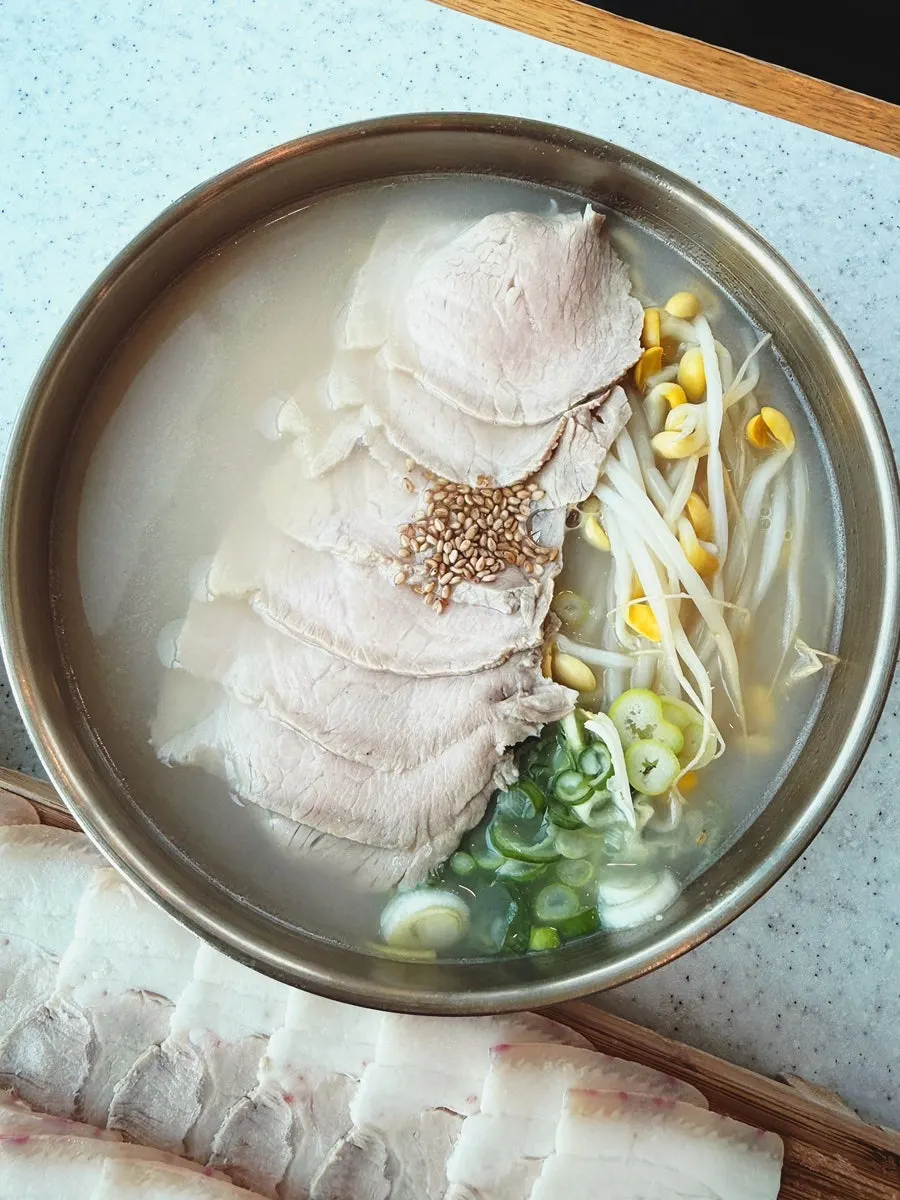 Table spread of rich bone broth pork noodles, dongchimi bibim noodles, and dombe naengsuyuk