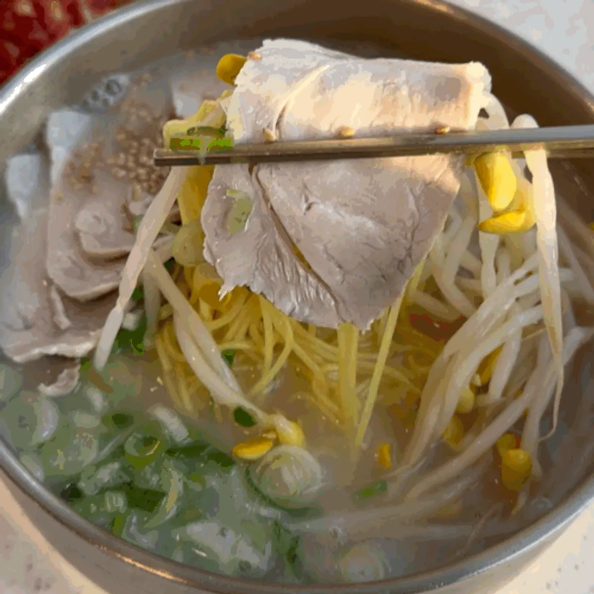 Pork noodle soup topped with bean sprouts, green onion, and pork