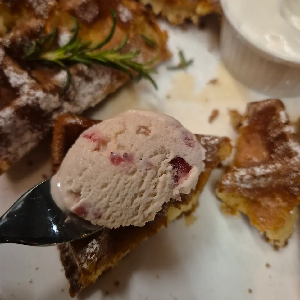 A waffle slice topped with strawberry and vanilla ice cream