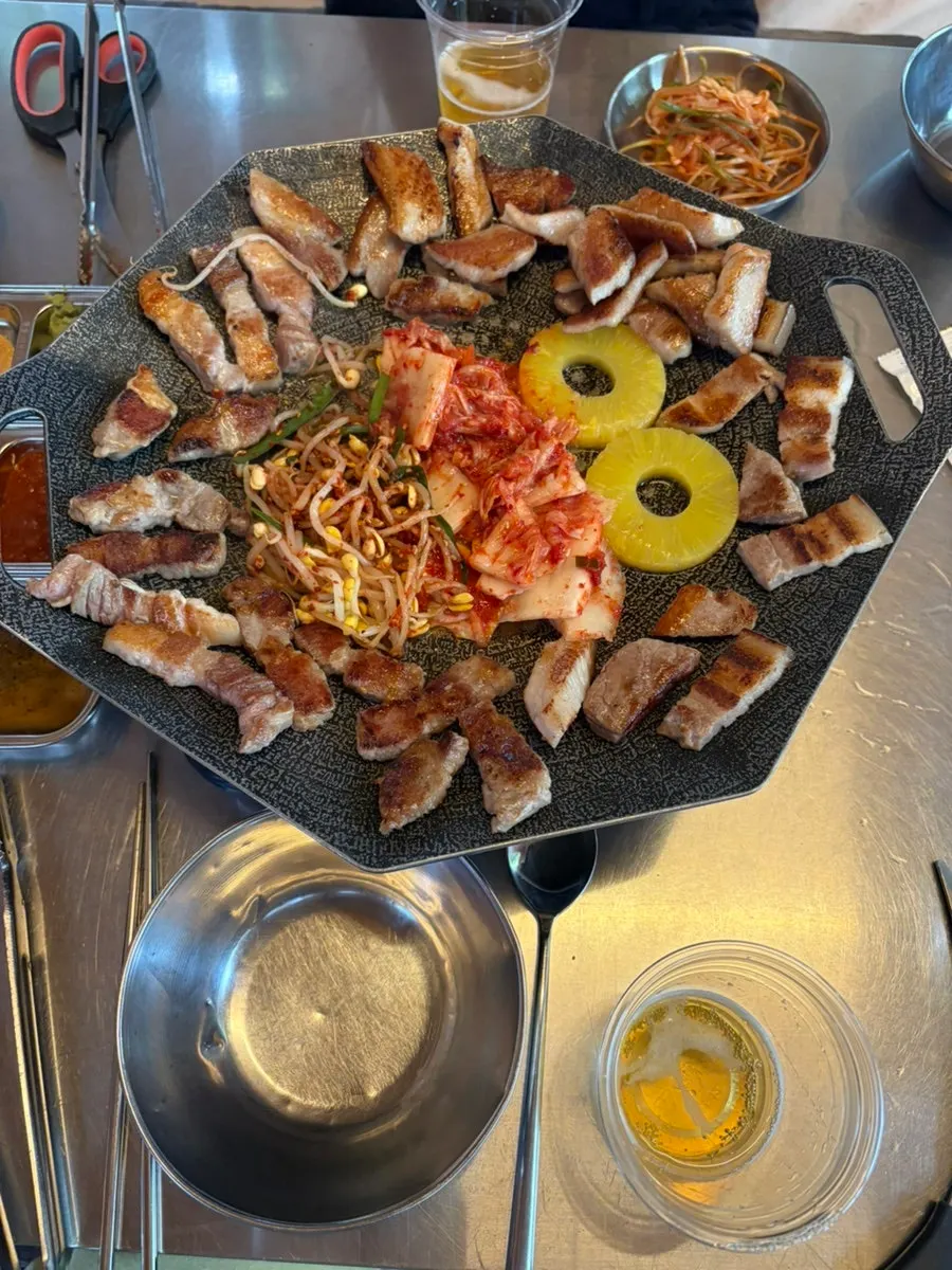 Meat grilling alongside pineapple, kimchi, and bean sprouts