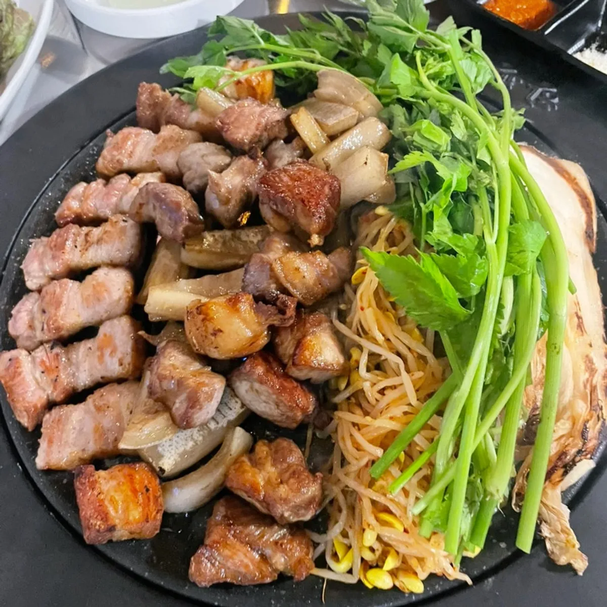 Grilled pork belly platter topped with bean sprouts and minari