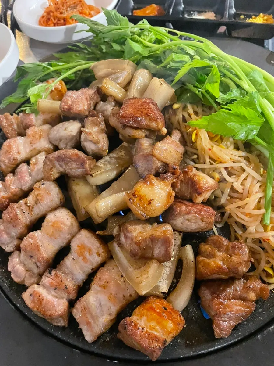 Thick cuts of pork with minari and kimchi on the hot plate