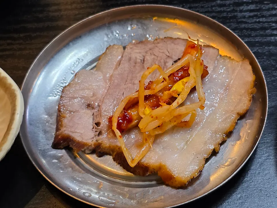 A piece of bossam topped with dried radish strips and bean sprout salad