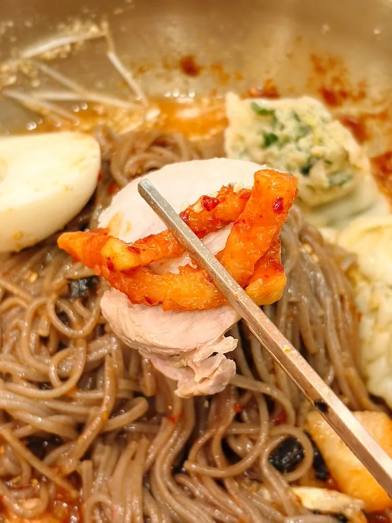 A bite of bibim makguksu topped with bossam and mu-saengchae