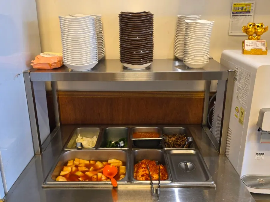 Self-serve side dish bar with diced radish kimchi and kimchi at Hanwoojang