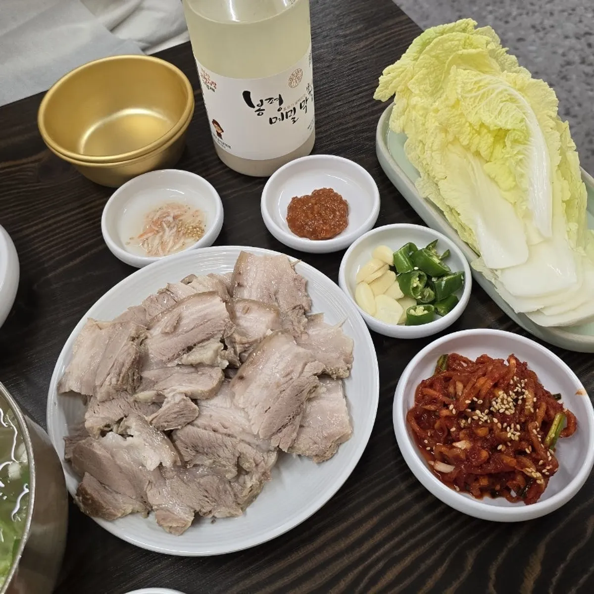 Bossam suyuk table setting with radish salad, cabbage, and Bongpyeong makgeolli