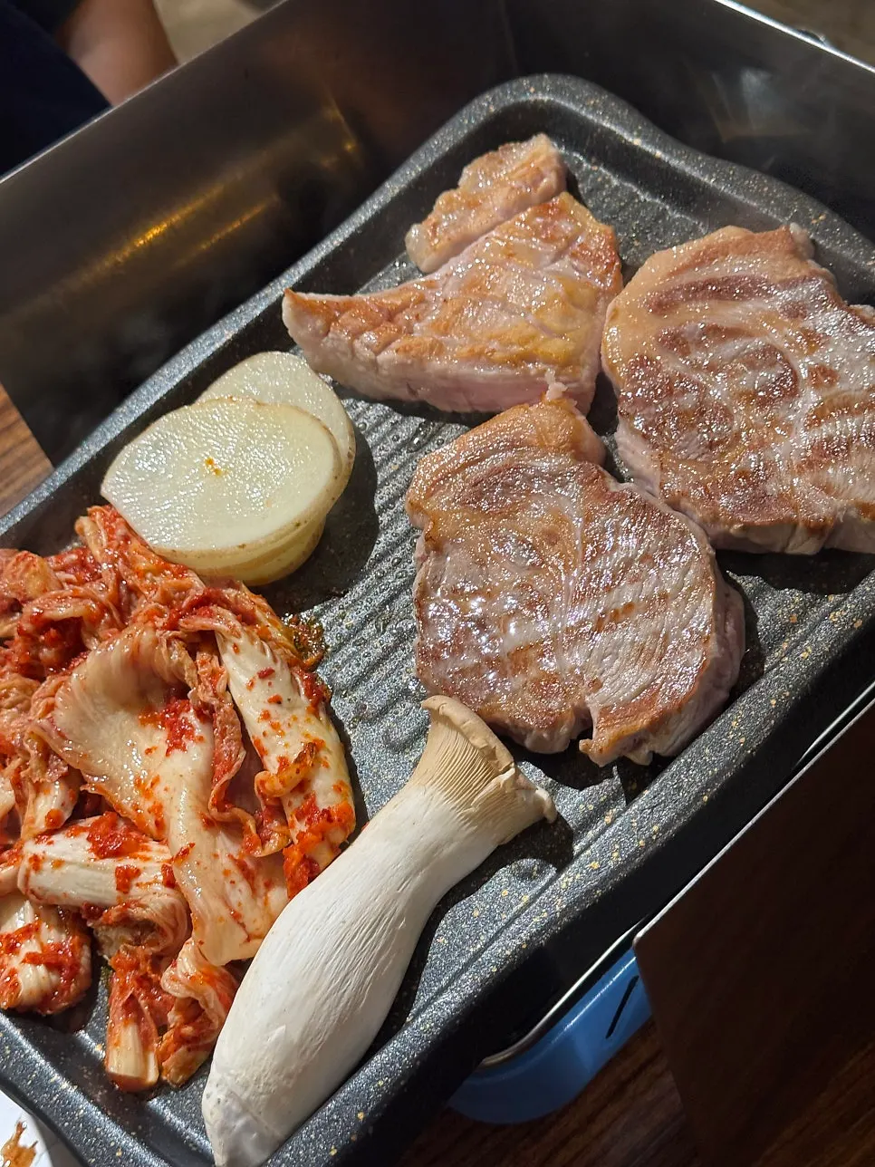 Meat grilling alongside potatoes and mushrooms