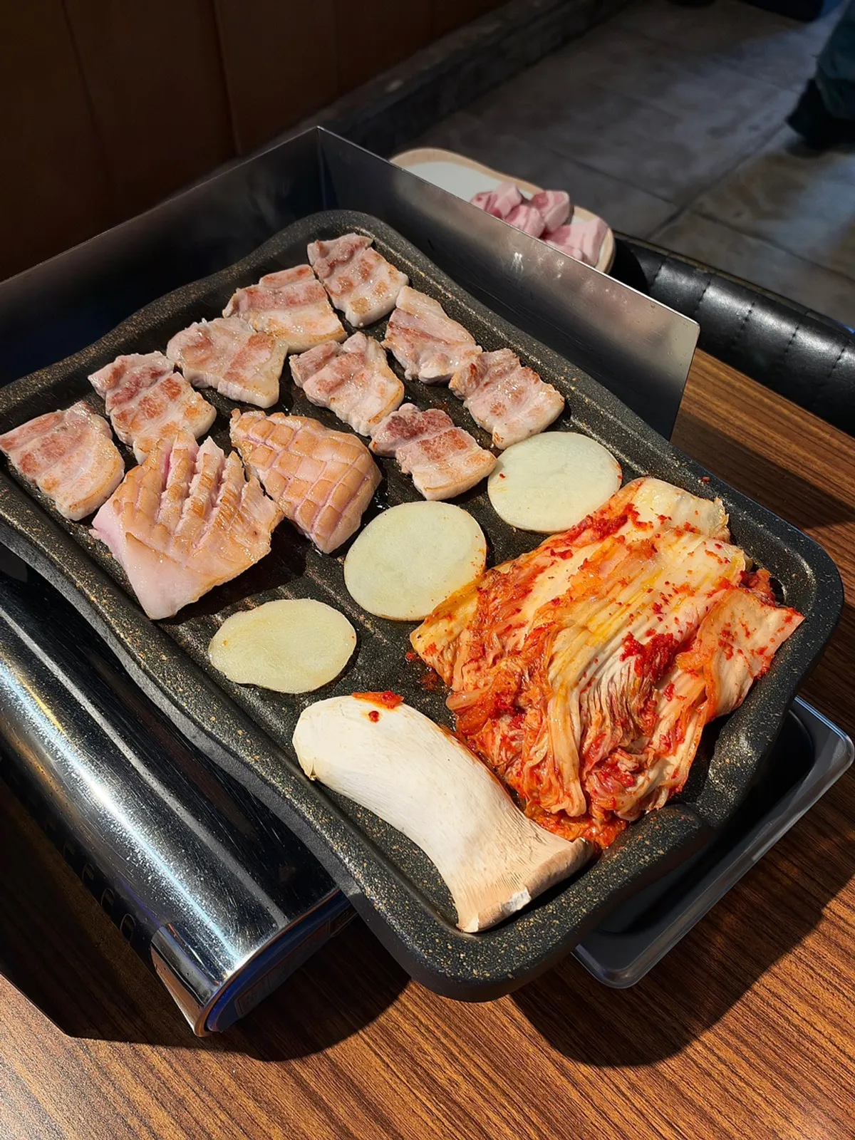 Pork belly grilling alongside aged kimchi on the hotplate