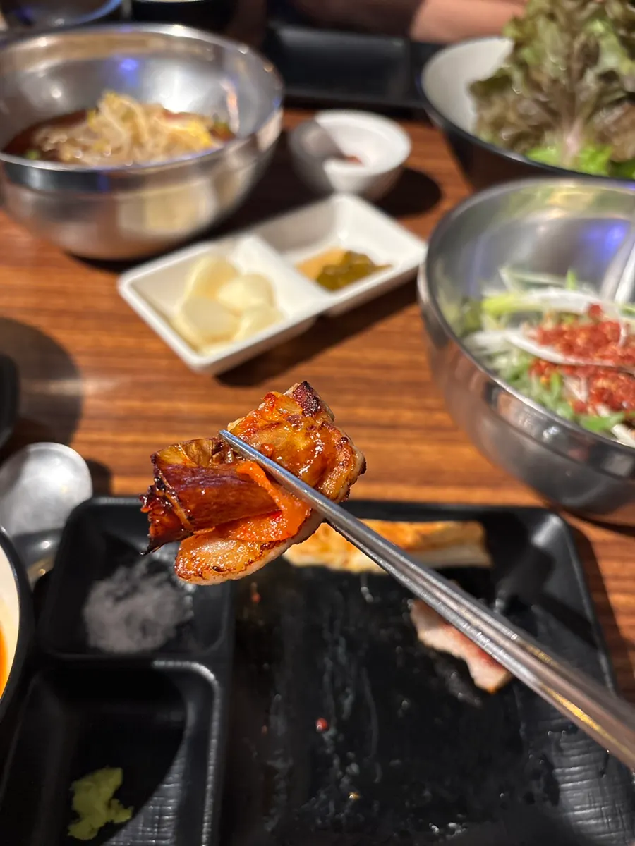 A lettuce wrap topped with meat, ssamjang, and aged kimchi