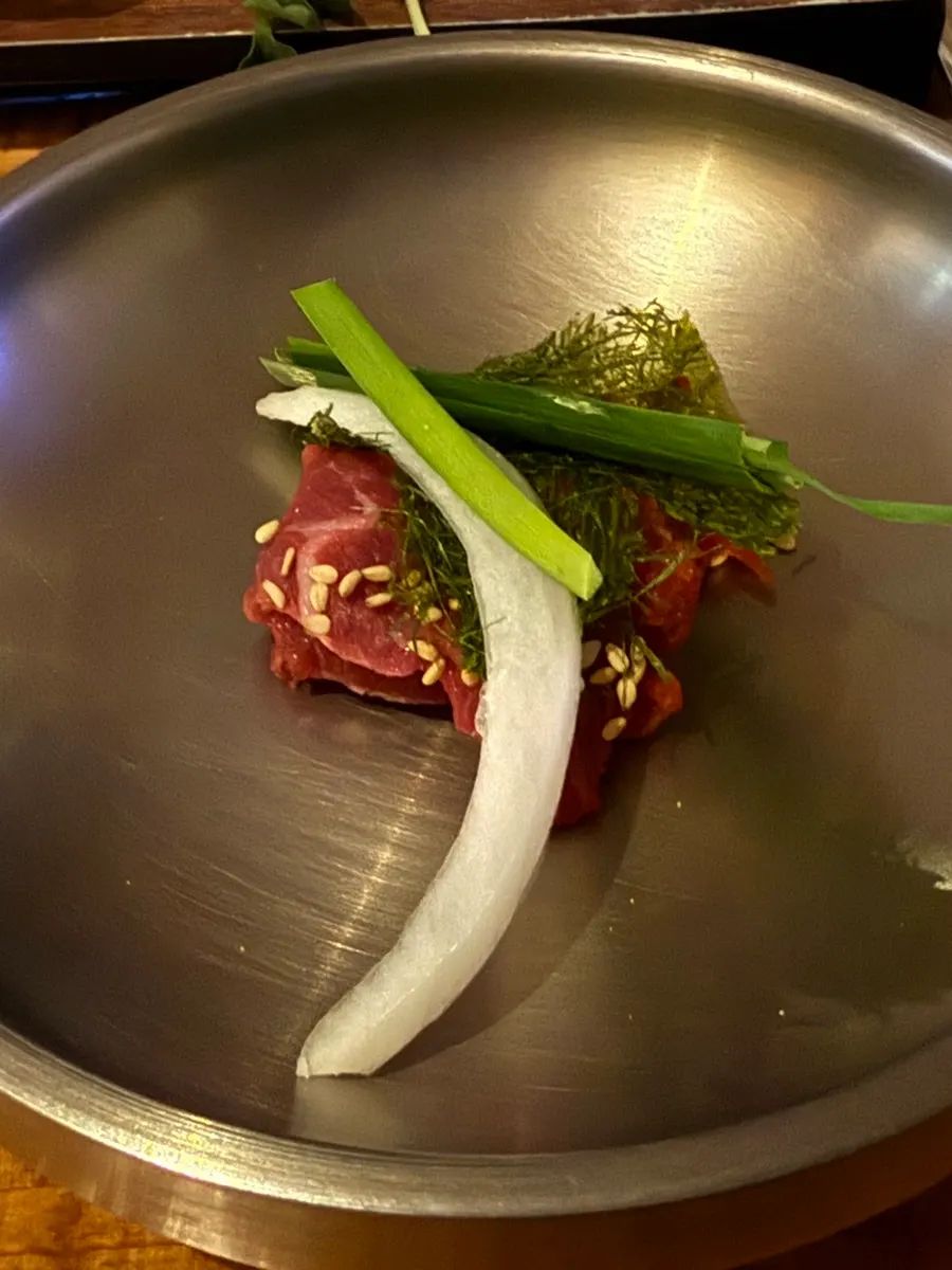 A piece of beef sashimi dipped in gochujang sauce